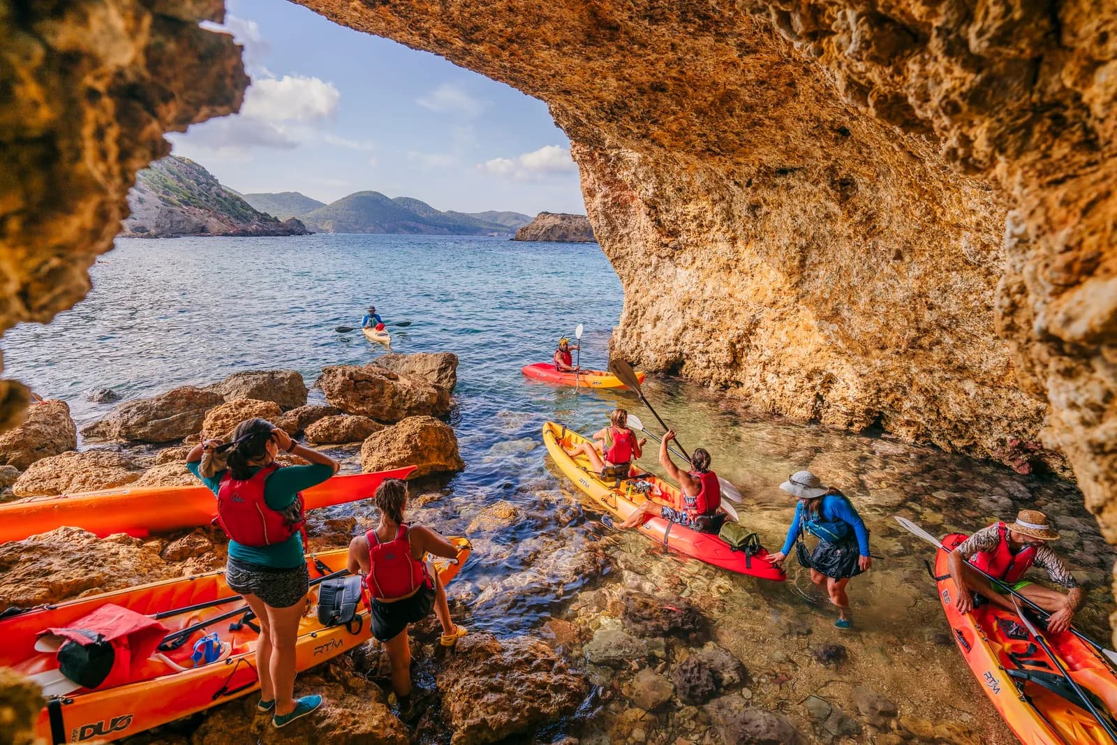 Group paddling rental sea kayaks over turquoise water in Ibiza
