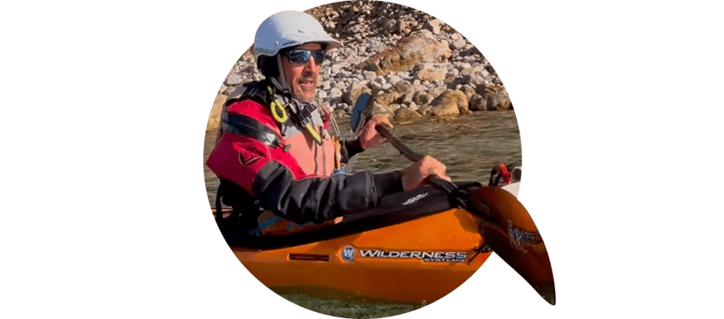 Hombre con casco y equipamiento completo de kayak remando en kayak naranja durante la temporada de otono e invierno en Ibiza