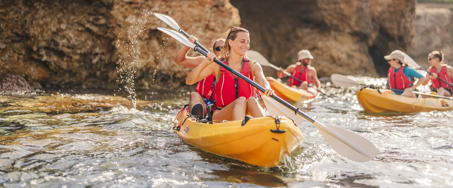 Kayak and snorkel tour group exploring Ibiza caves and cliffs with yellow kayaks in crystal clear waters.
