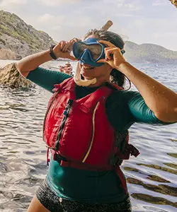 Woman adjusting snorkel mask and goggles while kayaking near rocky cliffs during kayak and snorkel tour in Ibiza