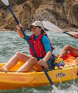 Happy woman celebrating with paddle raised while kayaking in yellow kayak during Ibiza kayak and snorkel adventure tour